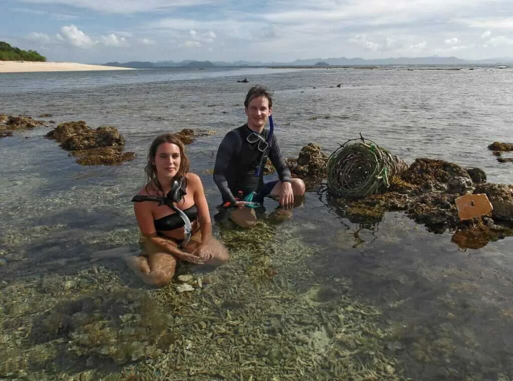 Two scuba divers sitting on rocks in shallow water.
