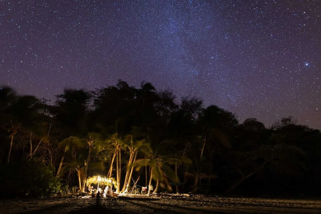 A group of people are sitting under the stars on a beach.