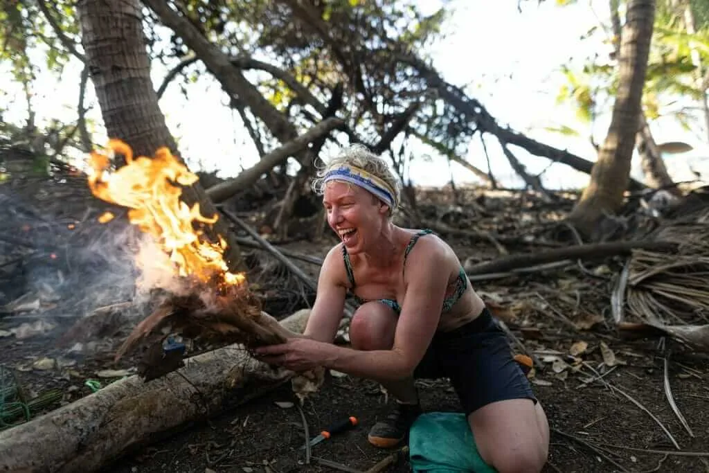 A woman kneeling down next to a fire in the woods.