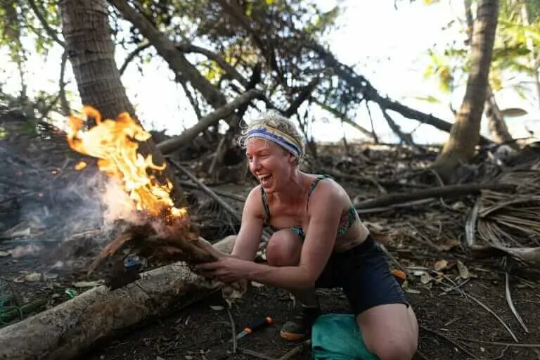 A woman kneeling down next to a fire in the woods.
