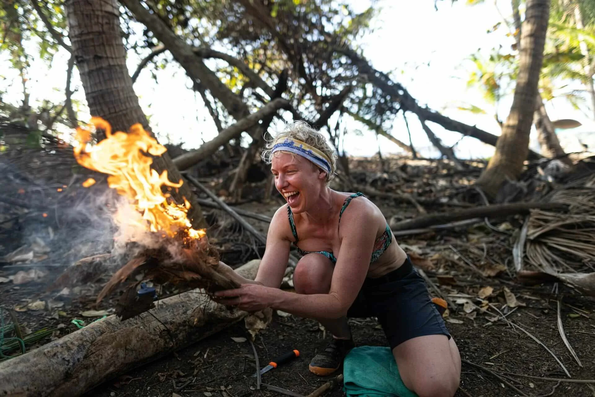A woman kneeling down next to a fire in the woods.