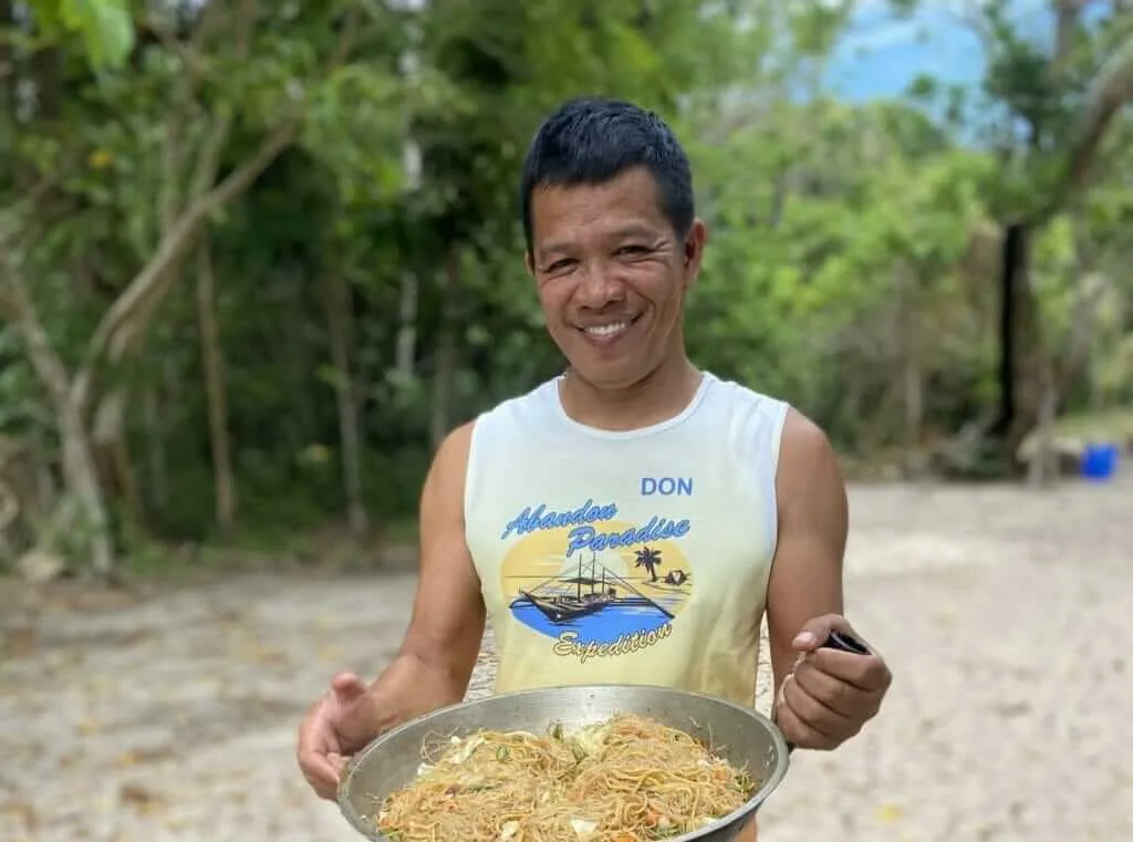 A man holding a plate of food on the beach.