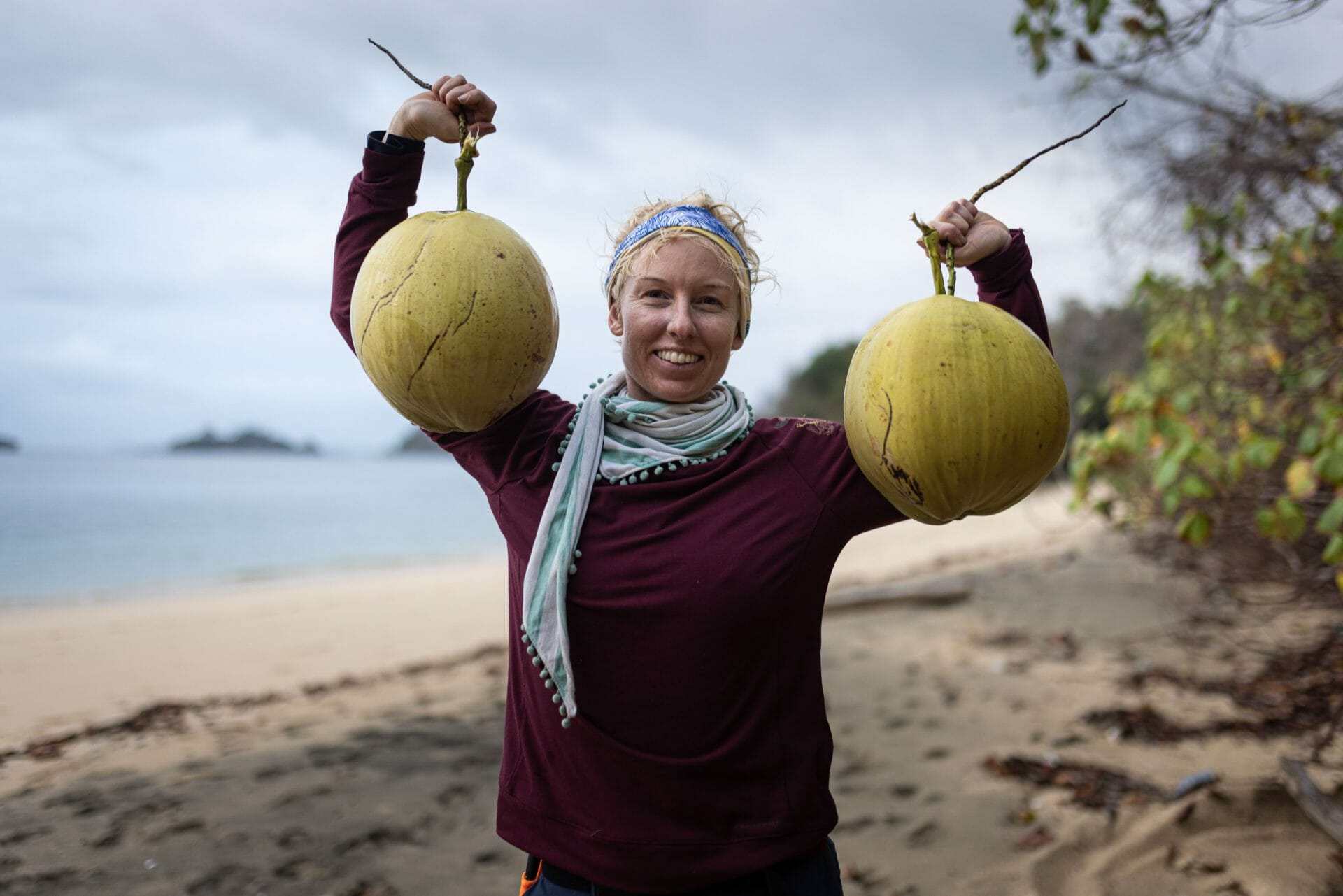 Woman holding up 2 coconuts on the beach