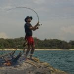 A man takes risks while standing on a rock with a fishing rod.
