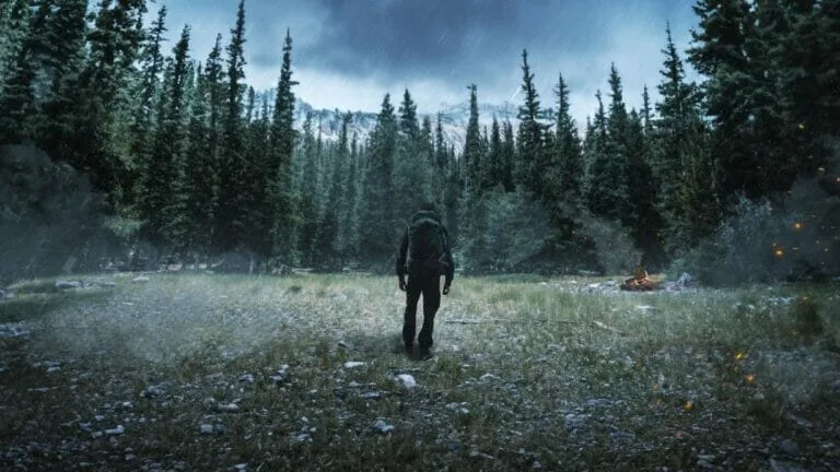 Alone in a forest clearing, a lone figure walks towards a campfire under a stormy sky. Alone UK Gear List.