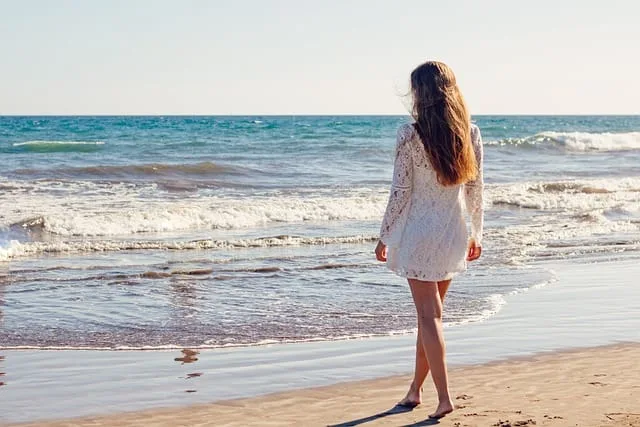 Woman in white dress walking on beach, a visual for a digital detox.