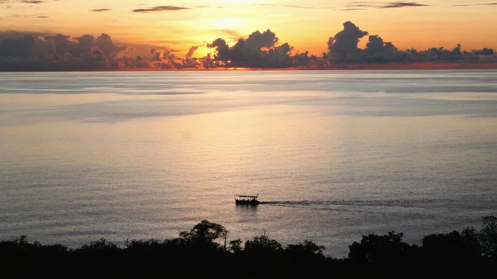 Boat sails on calm water under a vibrant sunset sky in Anambas, South China Sea.