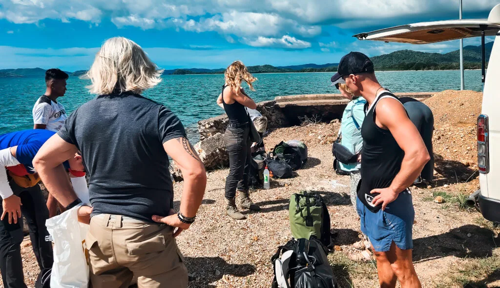 Group of people preparing for a Survivor-style adventure by the sea.
