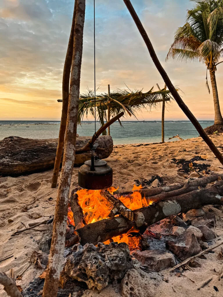 Beach campfire with kettle, evoking a 'Survivor' scene and survivor strategies for outdoor living.