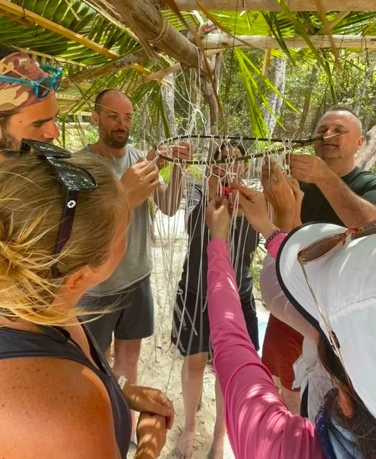 A group of people engaged in a team building activity, gathered around a string hanging from a tree.