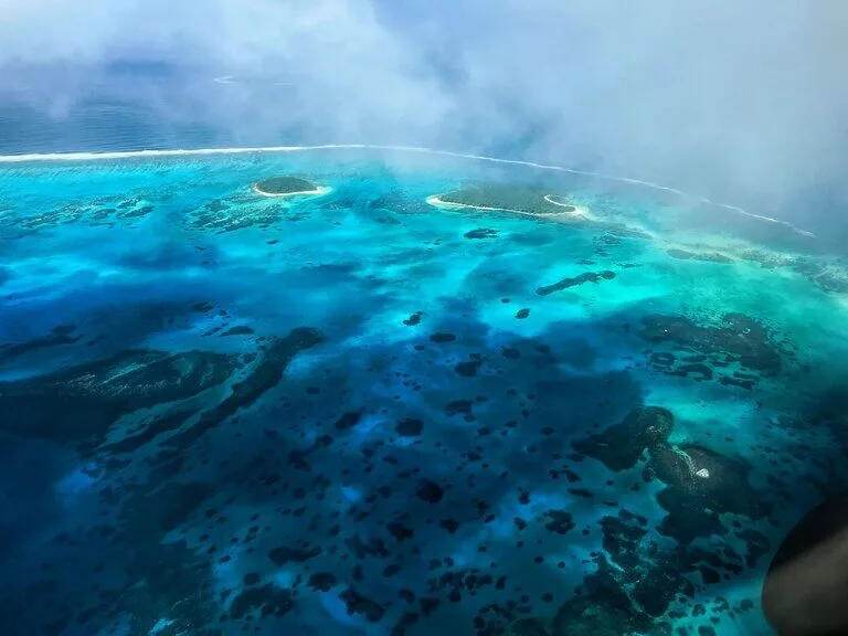 Aerial view of turquoise waters and small islands in Tonga, showcasing the beauty of Tonga in May.