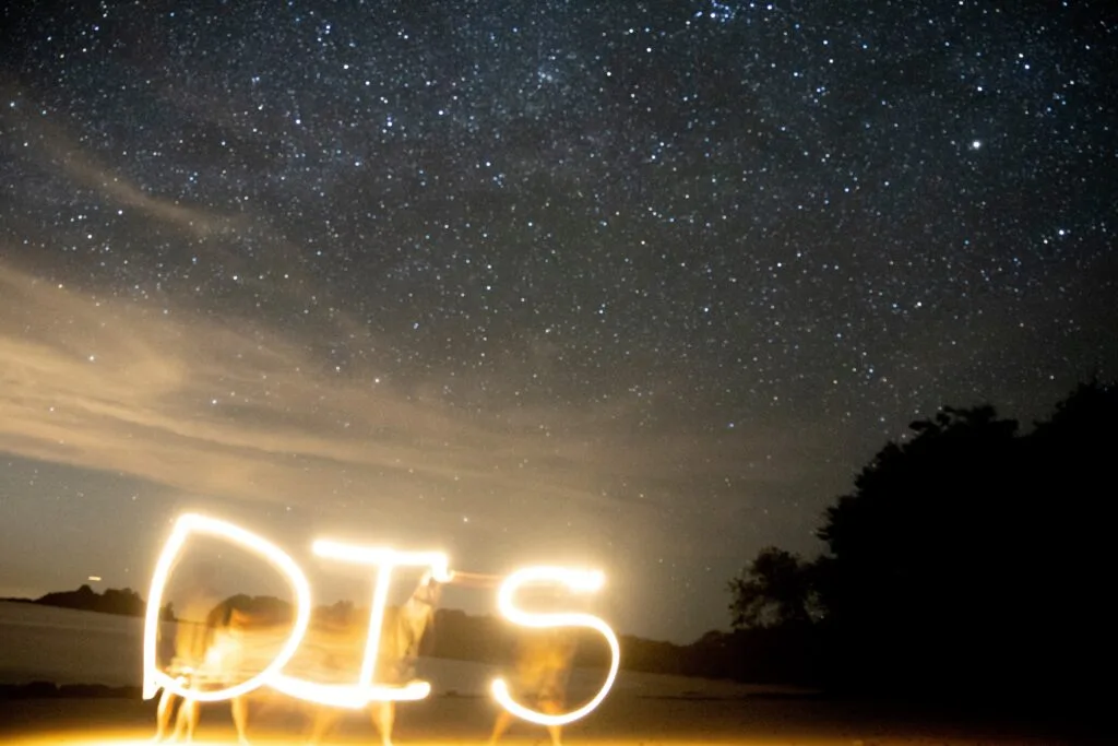 Team building exercise with light painting spelling "DIS" under a starry night sky.