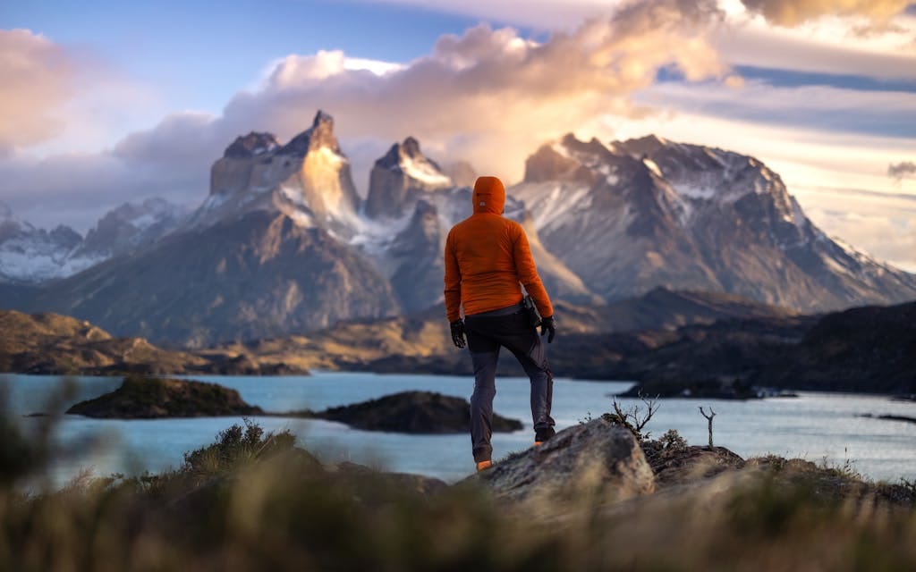 The Best Remote Holiday Destinations for Unforgettable Adventures 2 A hiker stands at sunrise in Torres del Paine, Chile, overlooking majestic mountains and a tranquil lake.