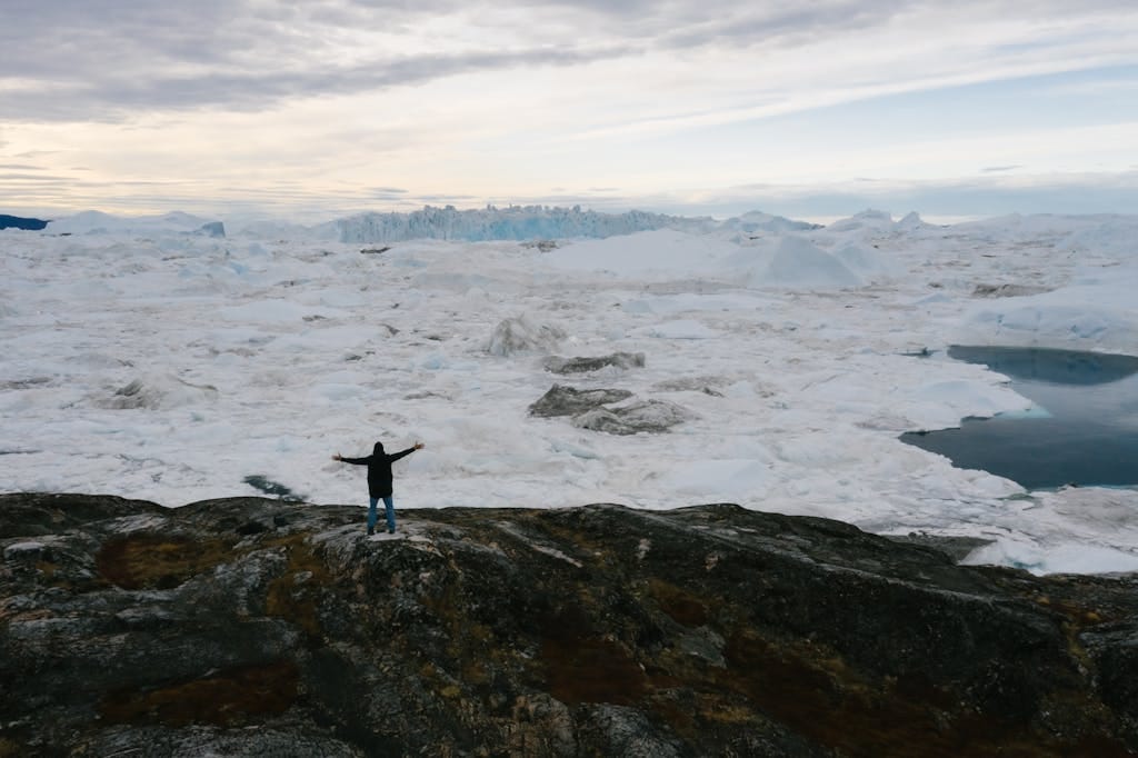 The Best Remote Holiday Destinations for Unforgettable Adventures 3 A lone figure with arms spread stands facing a vast frozen landscape, capturing a sense of adventure and solitude