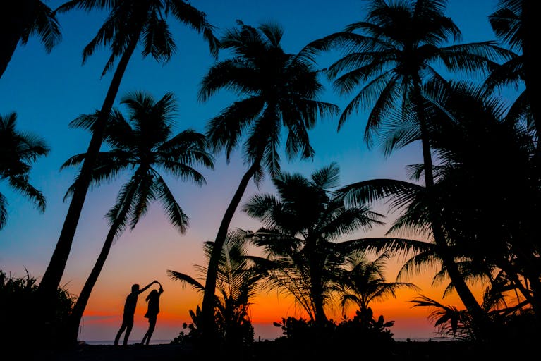 The Best Remote Holiday Destinations for Unforgettable Adventures 9 Silhouetted couple dancing under palm trees at tropical beach sunset, capturing romance and idyllic scenery.