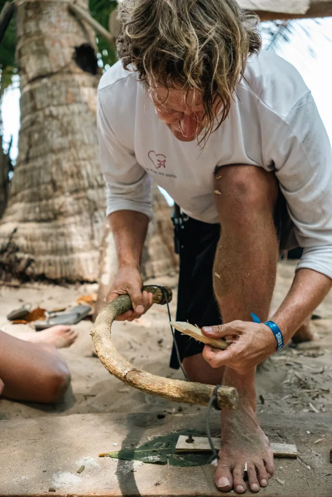 Man using a bow drill to start a fire on a beach. Survival skills demonstration.