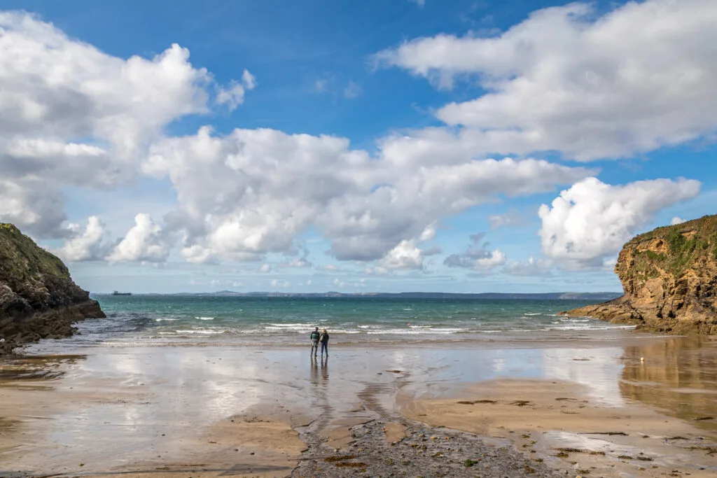 Couple on a sandy beach in Pembrokeshire under a cloudy sky.