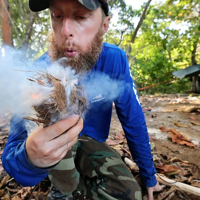 Man blowing on tinder bundle to start fire for Private Adventures.