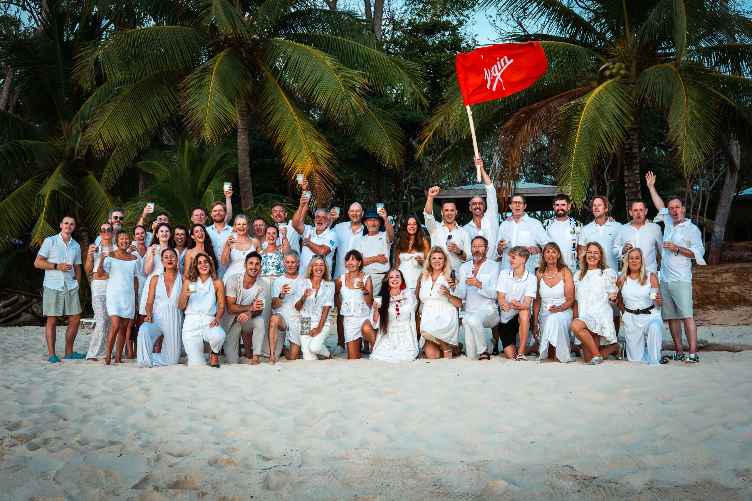 Group in white on a beach, holding a Virgin flag.