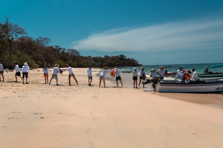 Group pulling boat onto sandy beach under a clear blue sky.