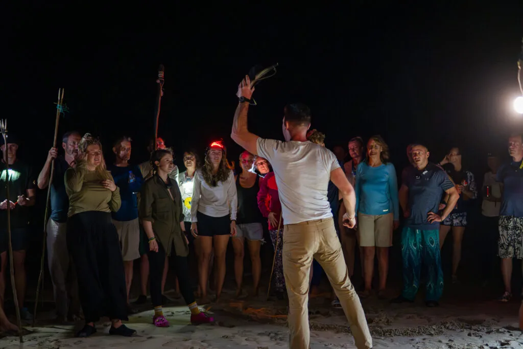 Group on beach at night, man raising object. Private Adventures tour.