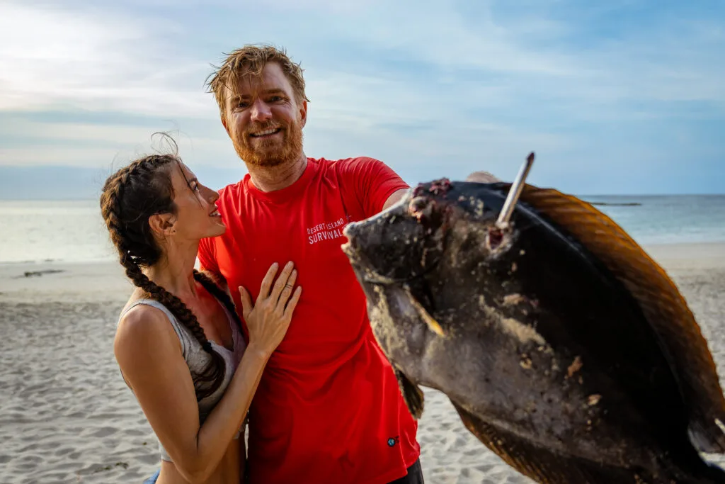 Couple on a beach with a large fish, possibly experiencing a day without technology.