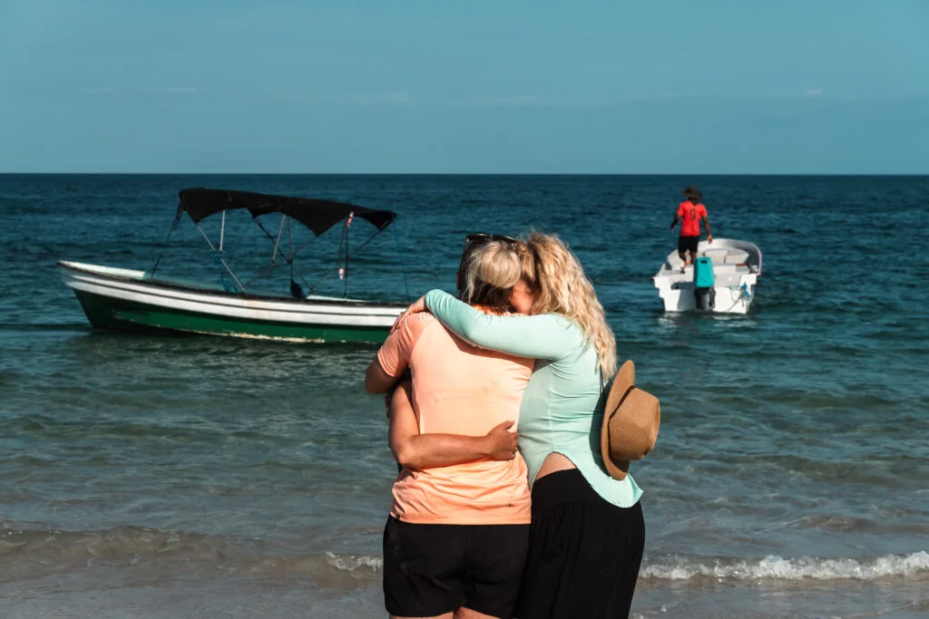 Two people embracing on a beach, boats in the background. A day without technology.