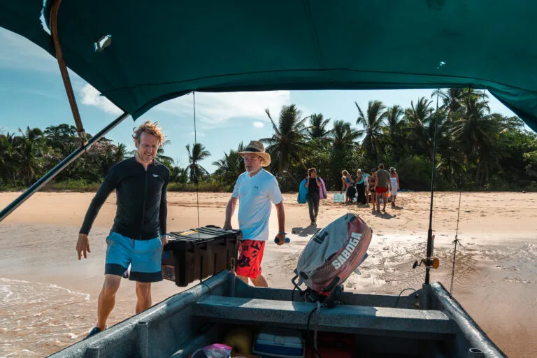 Men unloading gear from a boat onto a tropical beach for private adventures.
