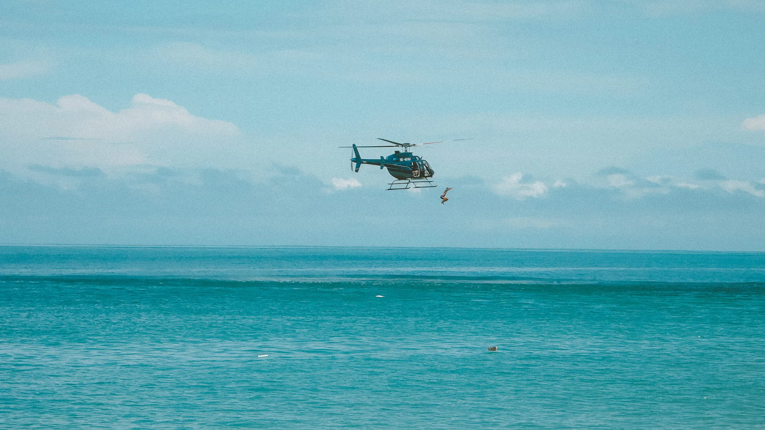Helicopter rescuing a person from the ocean, with blue sky and water.