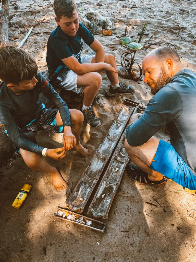 Kids learning survival skills with guide on sandy desert island, building fire with seashells and driftwood.