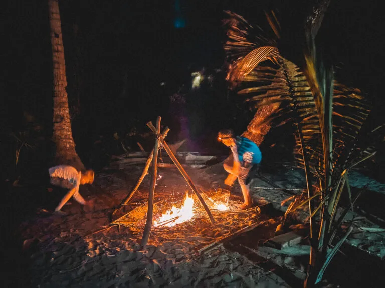 Survival skills on a deserted island, building a campfire at night for warmth and cooking.