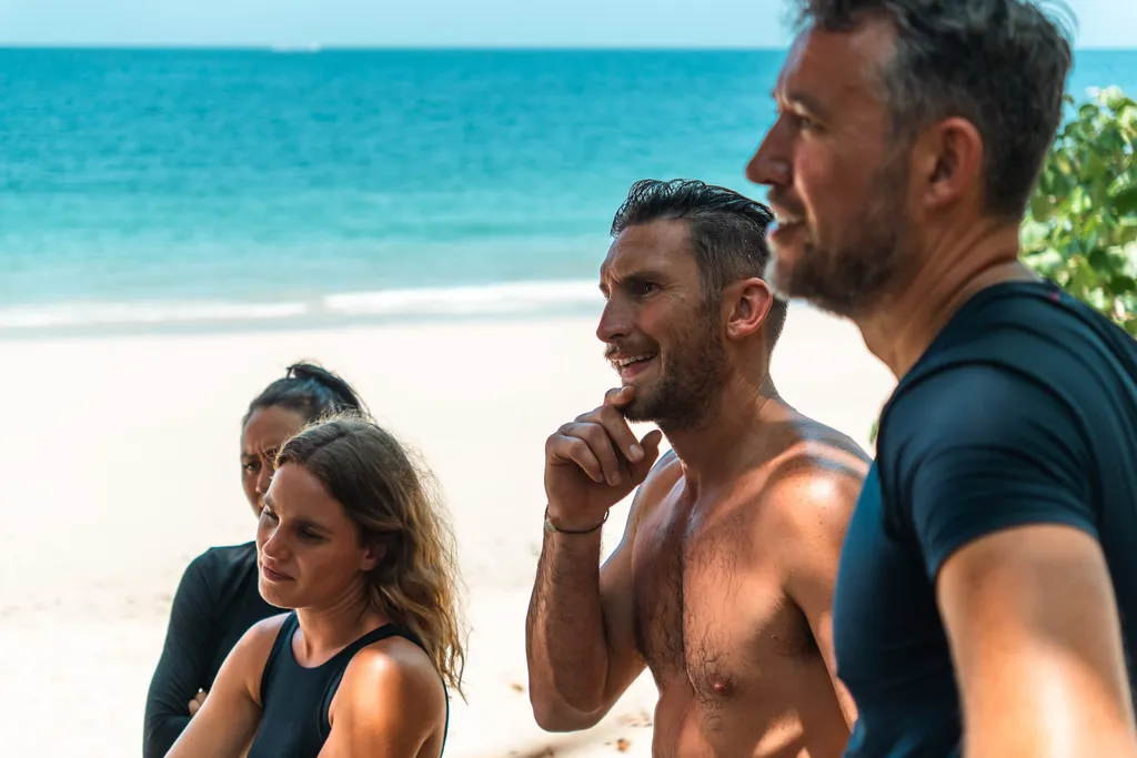 Survival experts discussing strategies on a tropical beach for a desert island survival challenge.