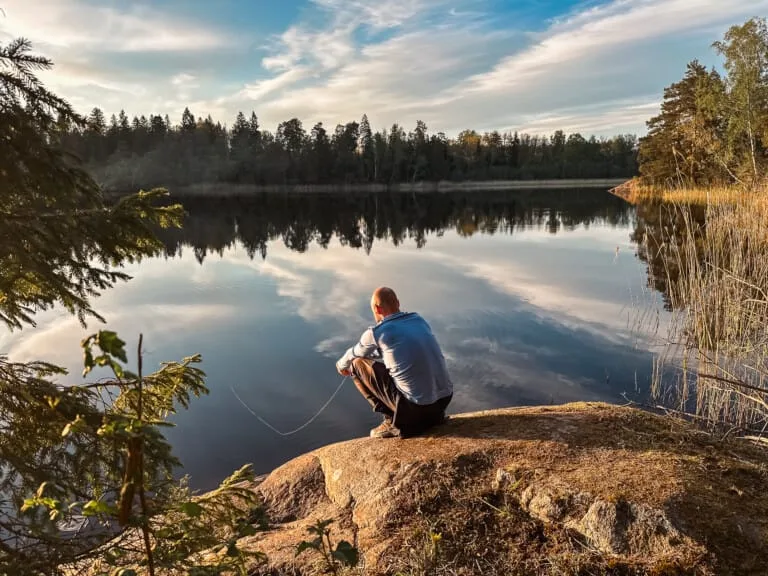 Man fishing at a serene lake in Sweden. Reflective water and peaceful landscape.