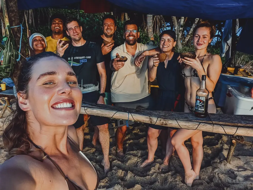 Desert Island Survival Adventure in Tonga 6 Survivors celebrating on a tropical desert island, enjoying coconuts and drinks, showcasing teamwork and survival skills in a wilderness setting, perfect for desert island survival adventures and outdoor challenges.