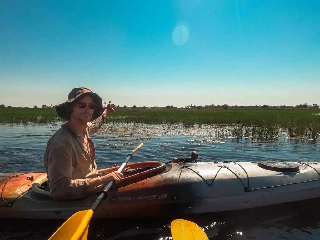 Botswana Kayak Bushcraft Safari in the Okavango Delta 8 Survival kayaking on a remote desert island, featuring a person with kayaking gear exploring marshland, emphasizing wilderness survival skills and outdoor adventure in a tropical environment.