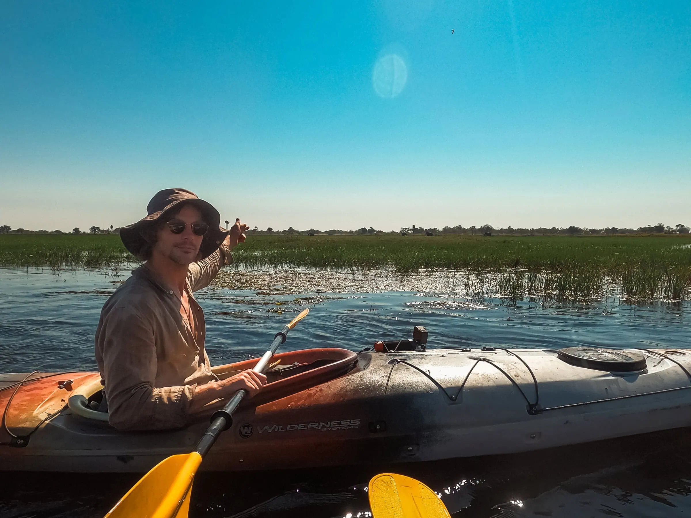 Botswana Kayak Bushcraft Safari in the Okavango Delta 20 Survival kayaking on a remote desert island, featuring a person with kayaking gear exploring marshland, emphasizing wilderness survival skills and outdoor adventure in a tropical environment.