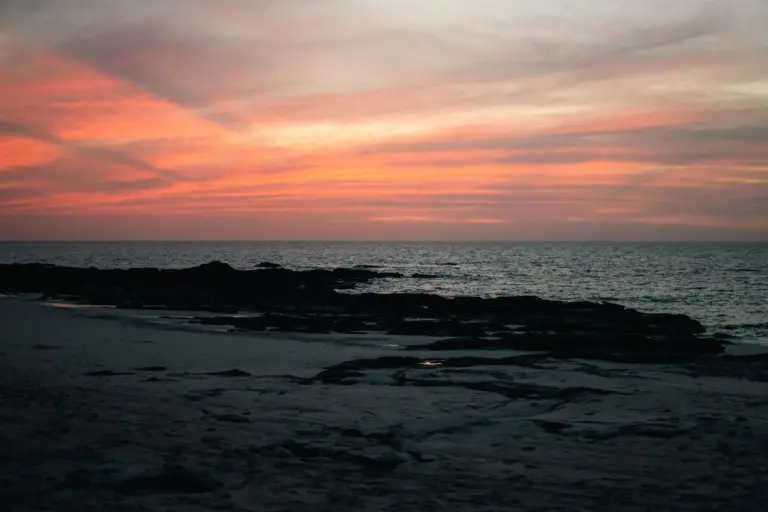 What Happens on a Desert Island (That You'll Carry Forever) 1 Vibrant sunset over a deserted beach with rocky shoreline, ideal for desert island survival scenarios, emphasizing ocean, nature, and outdoor adventure.
