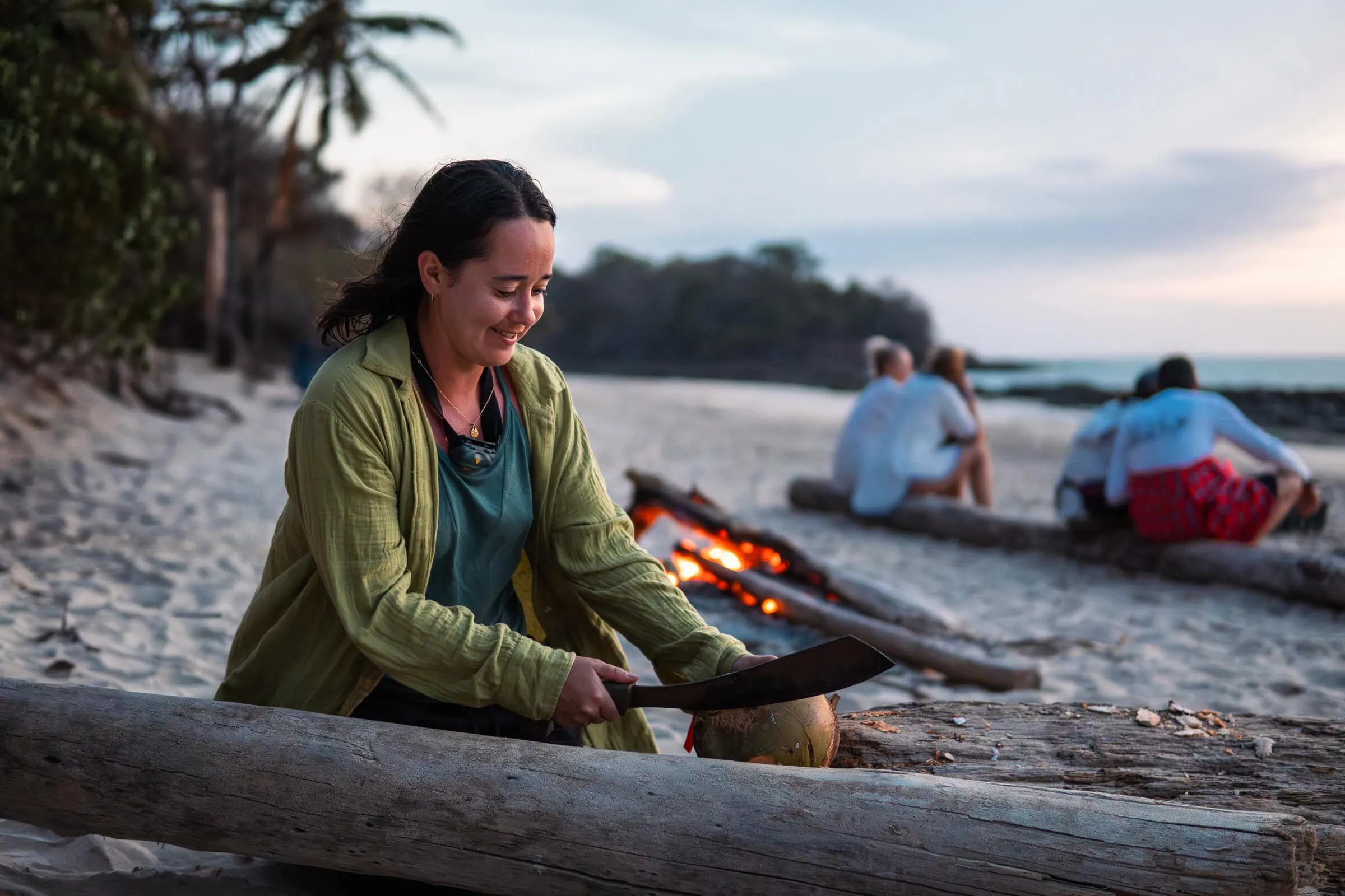 An Adventurer on a Desert Island, learning survival skills, building a fire, exploring survival techniques, beach setting with palm trees, sand, and ocean in the background.