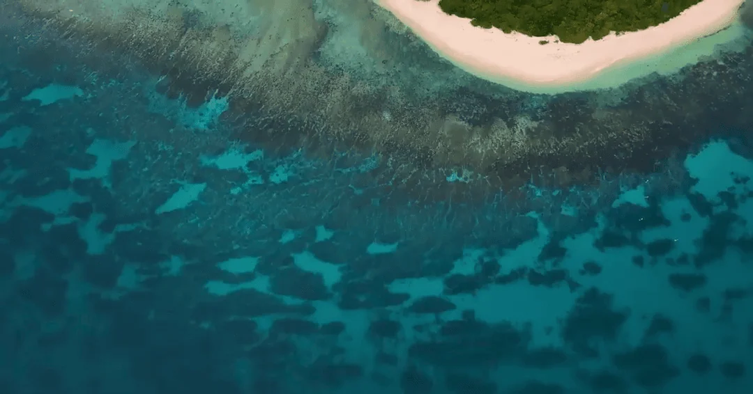 Colorful aerial view of a deserted tropical island surrounded by crystal-clear blue ocean waters, showcasing a perfect location for survival, adventure, and island exploration.