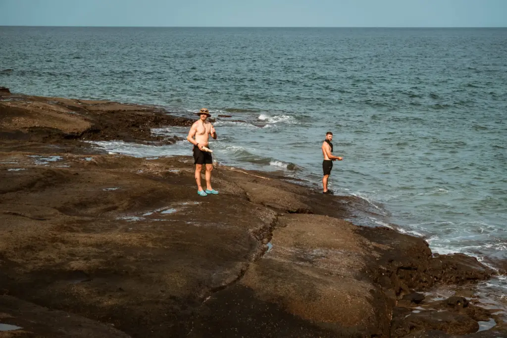 Two men fishing on a rocky coast, embodying the real risk in survival training.