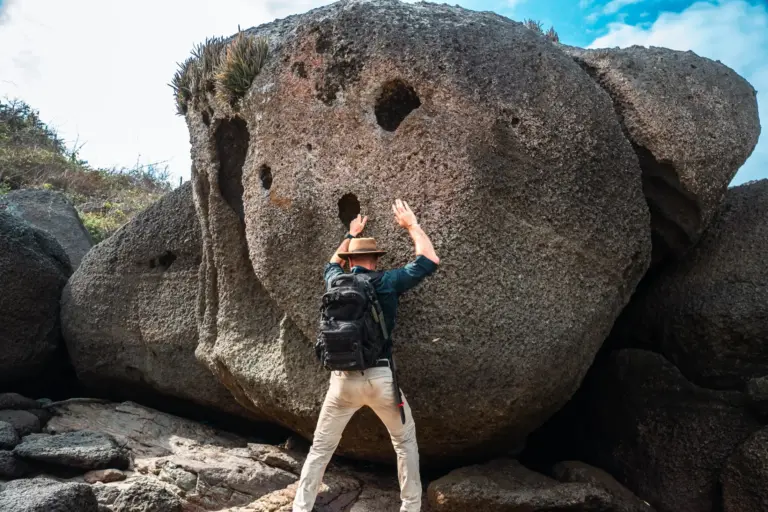 Man with backpack near large rock formation with holes, reaching up