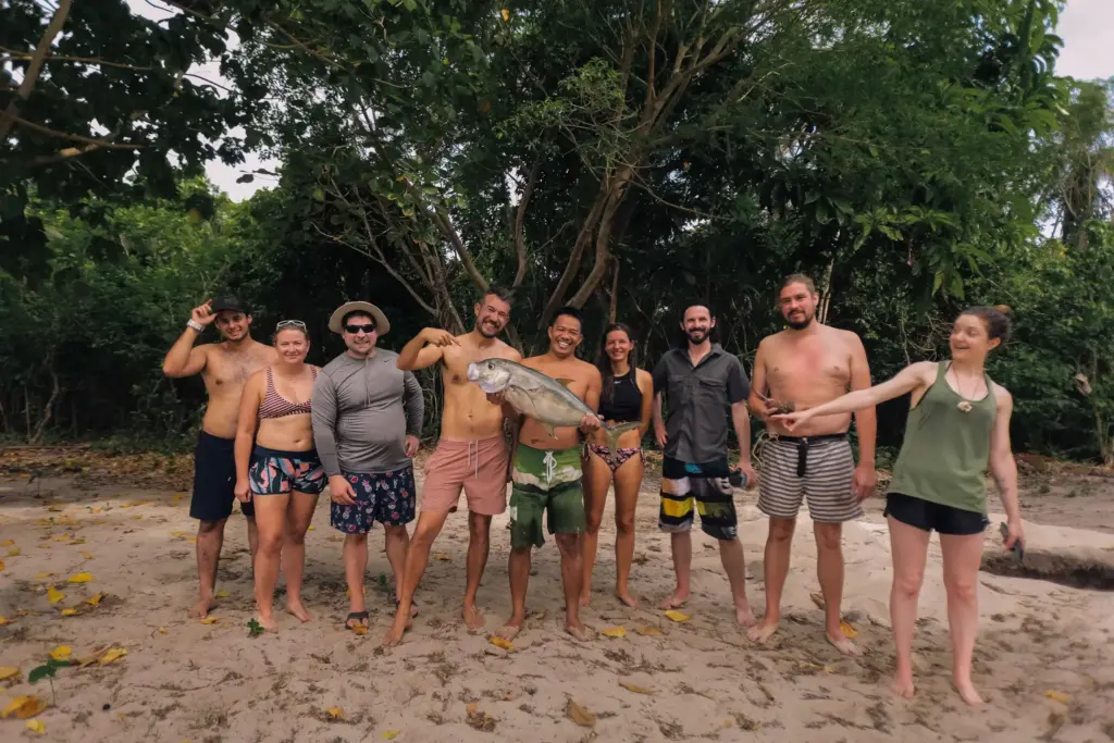 Group of people on beach holding a fish, tropical setting.