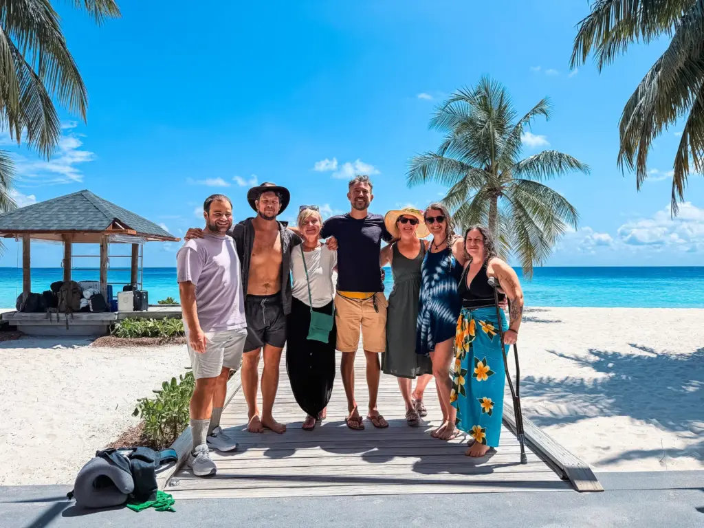 Group poses on beach in the Maldives with turquoise water and palm trees.