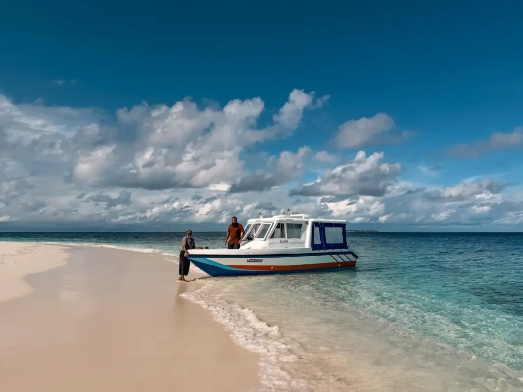 Two people by boat on a tropical beach in the Maldives. Clear turquoise water.