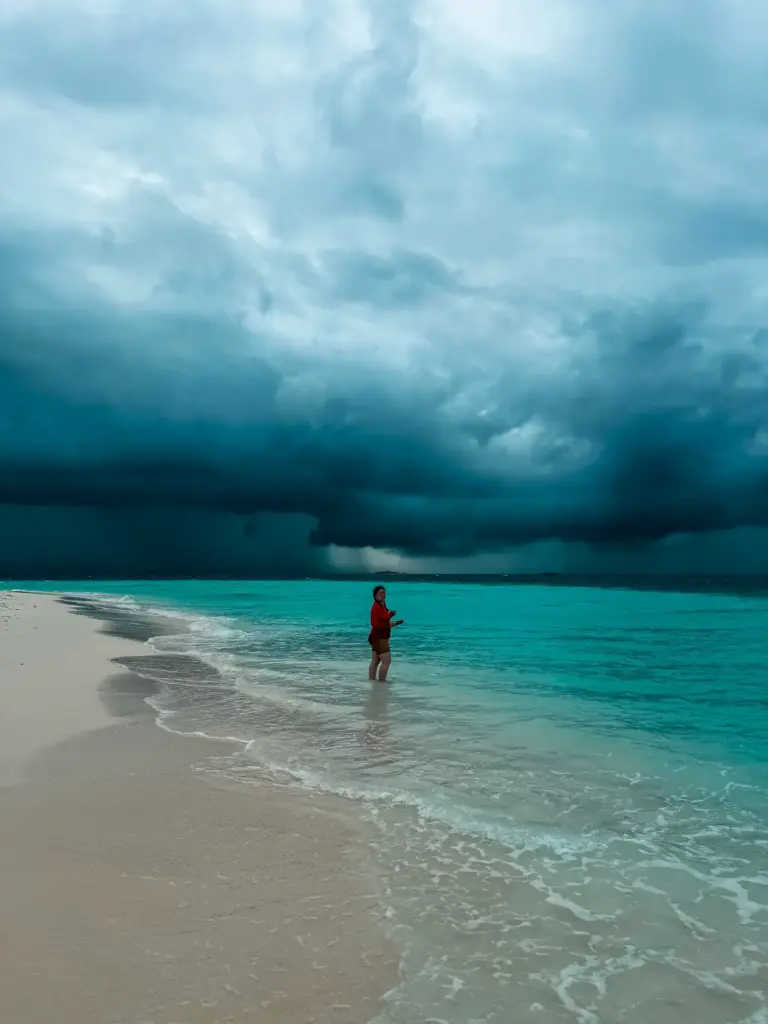 Person stands in turquoise water on a Maldives beach under stormy skies.
