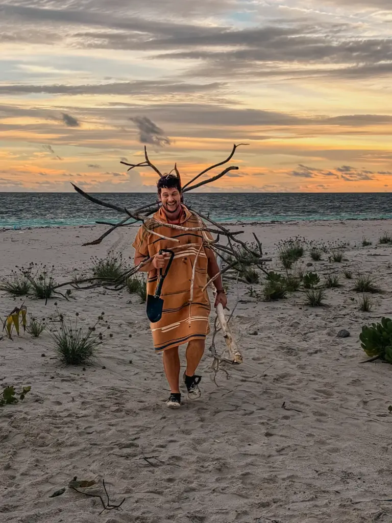 Man carrying driftwood on a beach in the Maldives at sunset.
