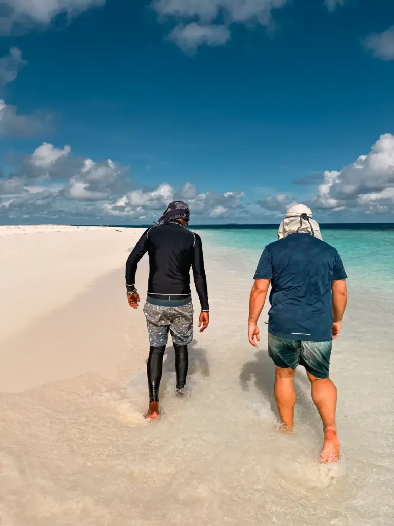 Two men walking on a white sand beach in the Maldives. Turquoise water.