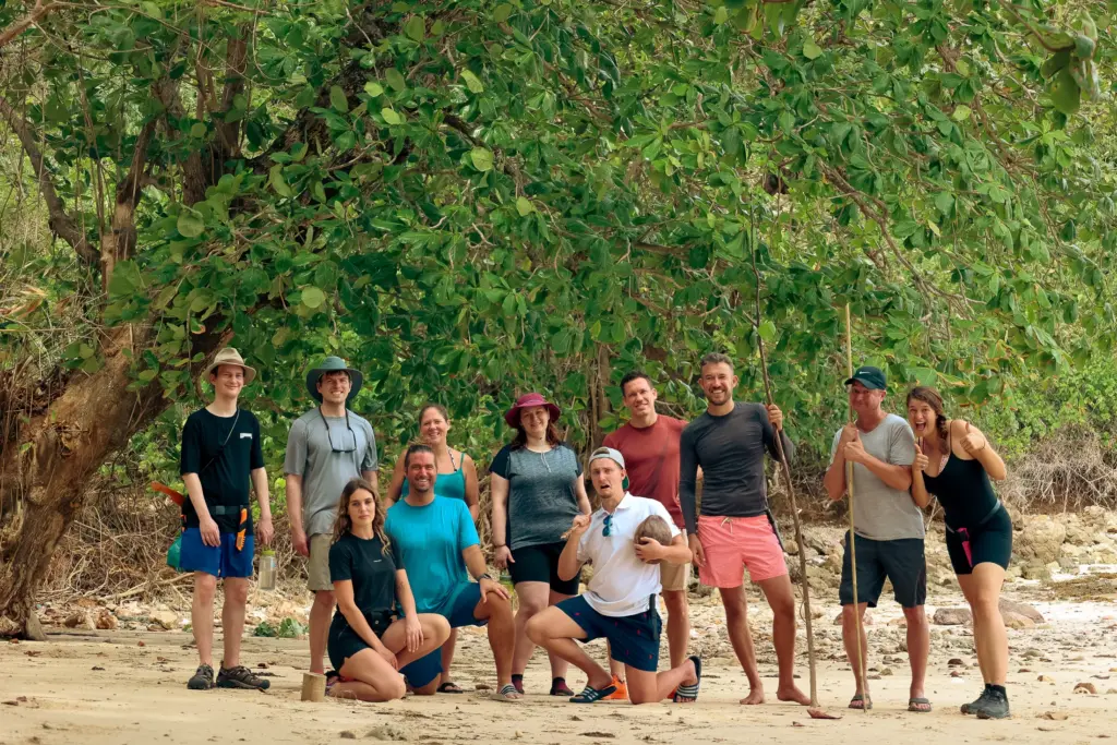 Group of people on a beach survival expedition, posing under a tree.