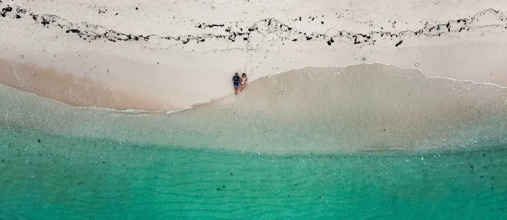 Couple walking on a tropical beach with turquoise water and white sand. Ocean view.