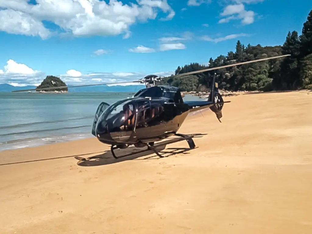 Black helicopter on sandy beach with island and blue sky. Abel Tasman National Park, New Zealand.